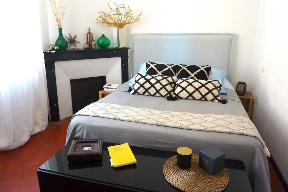 Une chambre à coucher bien aménagée, avec un lit, des tables de chevet, une petite cheminée et des objets décoratifs.