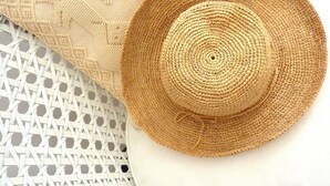 Un sombrero de paja con un diseño circular, sobre un almohadón blanco de textura tejida.