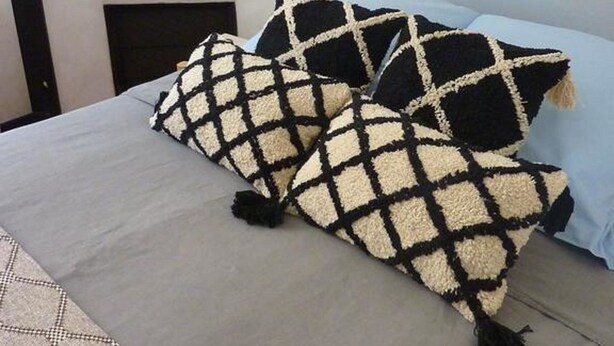 Una cama con una colcha gris y dos almohadas estampadas en blanco y negro.