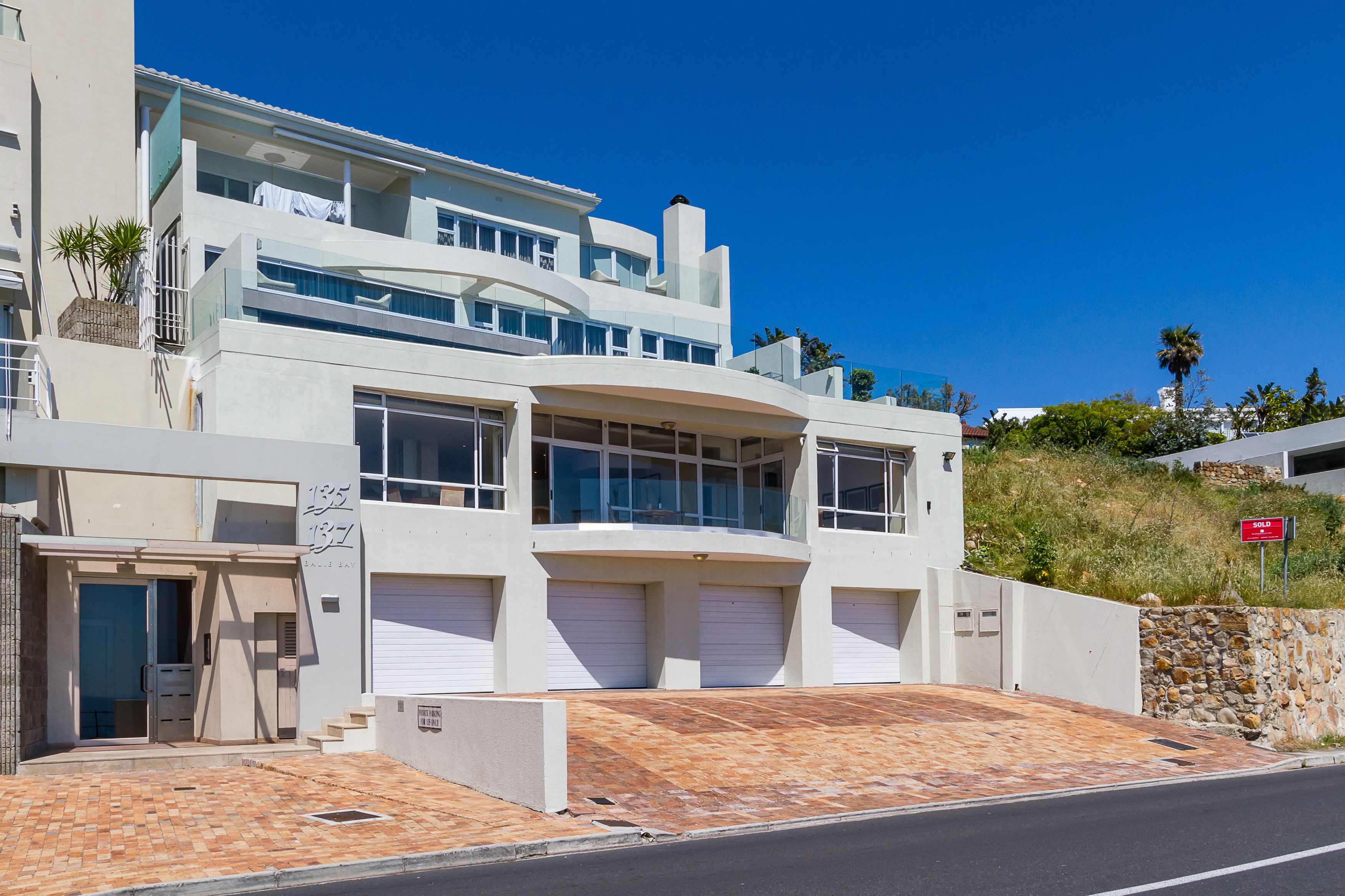 Ein modernes, mehrstöckiges Gebäude mit Garage, einer Steinmauer und blauem Himmel.