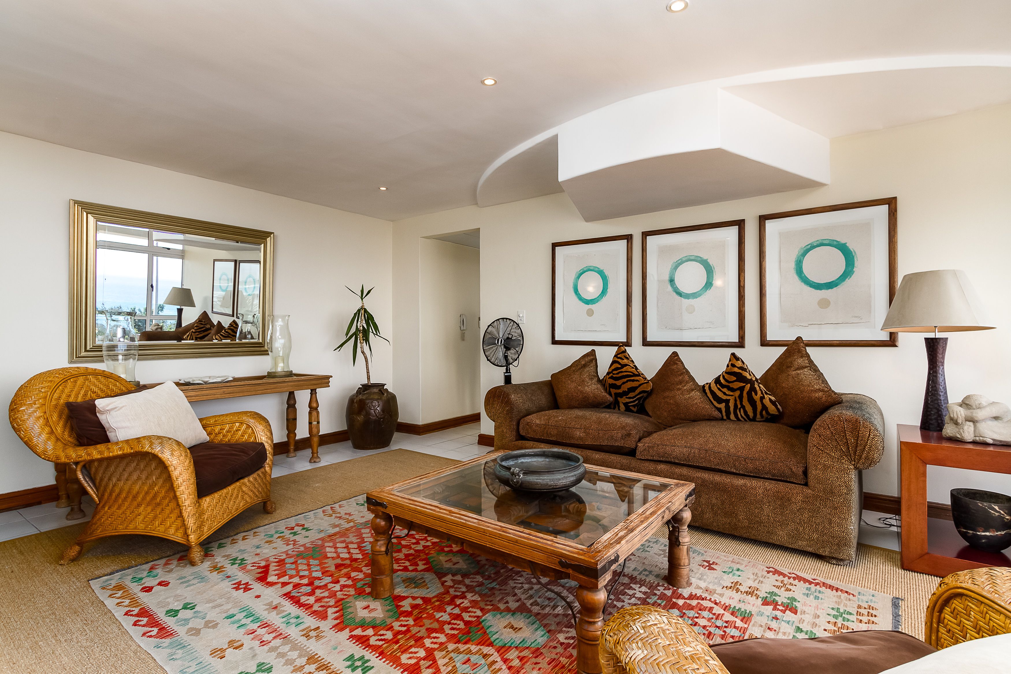A living room with a wicker chair, a brown sofa, a glass coffee table, and a patterned rug.