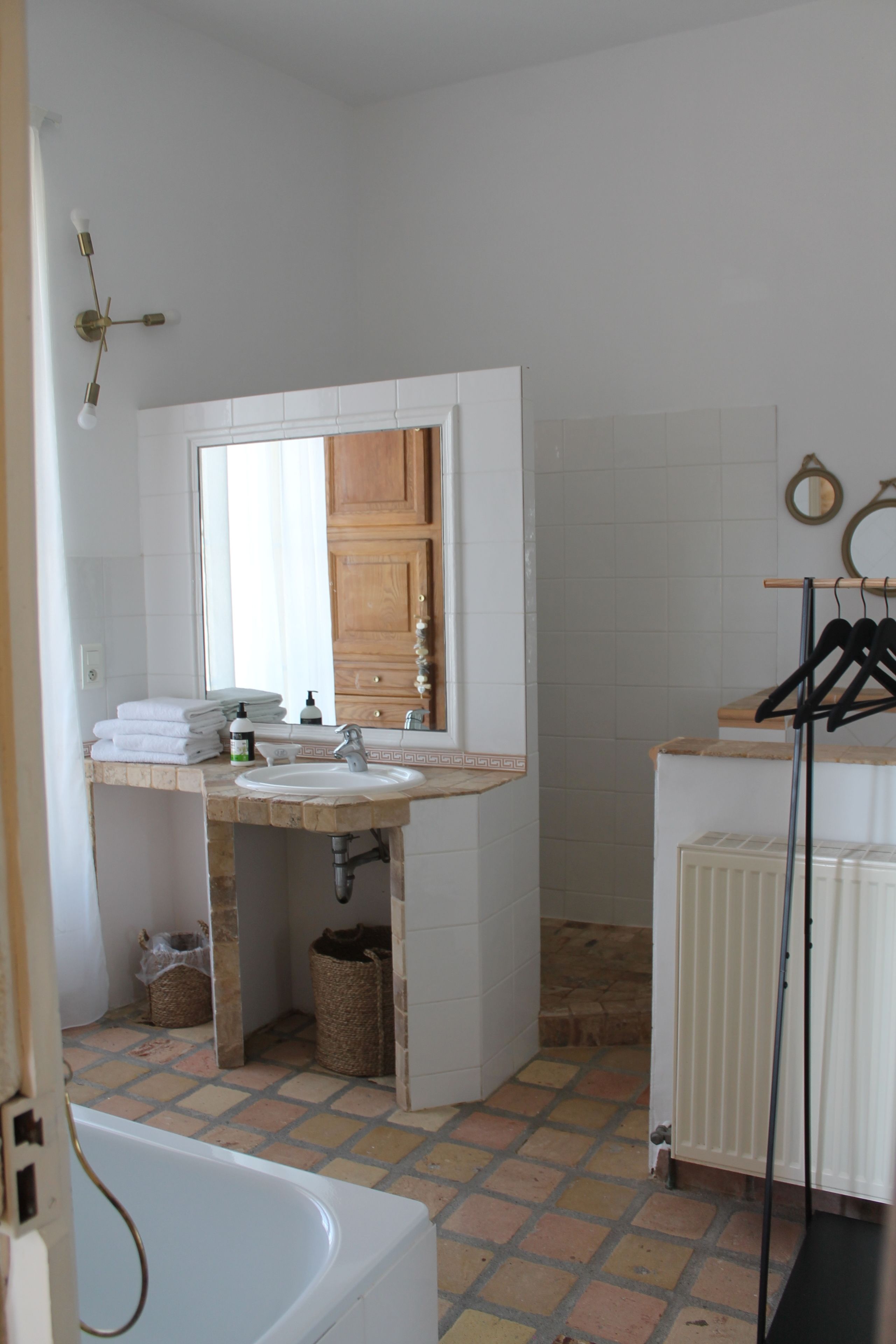 Une salle de bain avec une baignoire, un lavabo et un miroir. Des serviettes sont pliées sur le comptoir, et un étendoir à vêtements est suspendu.