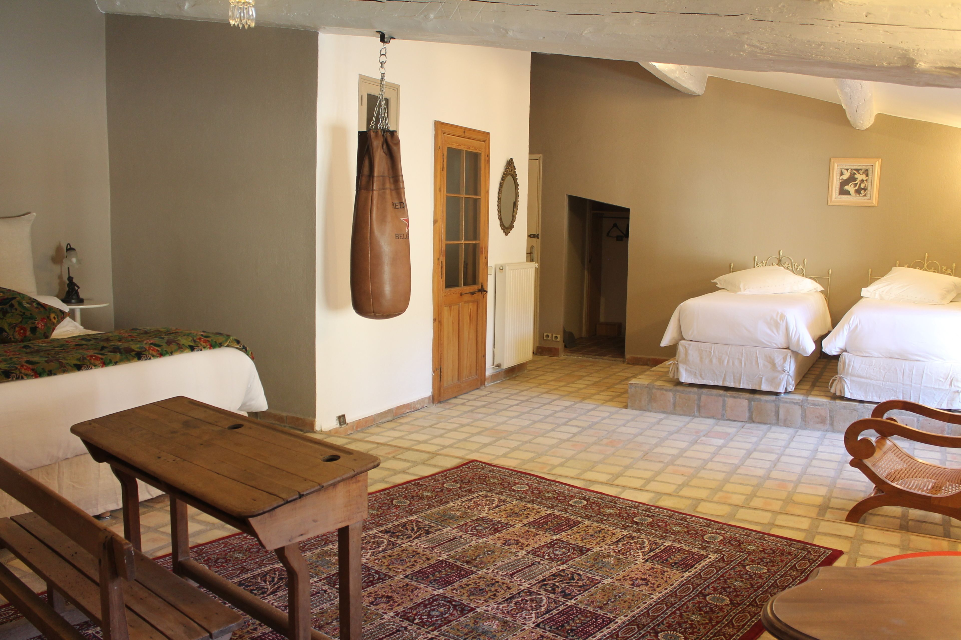 A room with a bed, a wooden table, a punching bag, and two white beds.