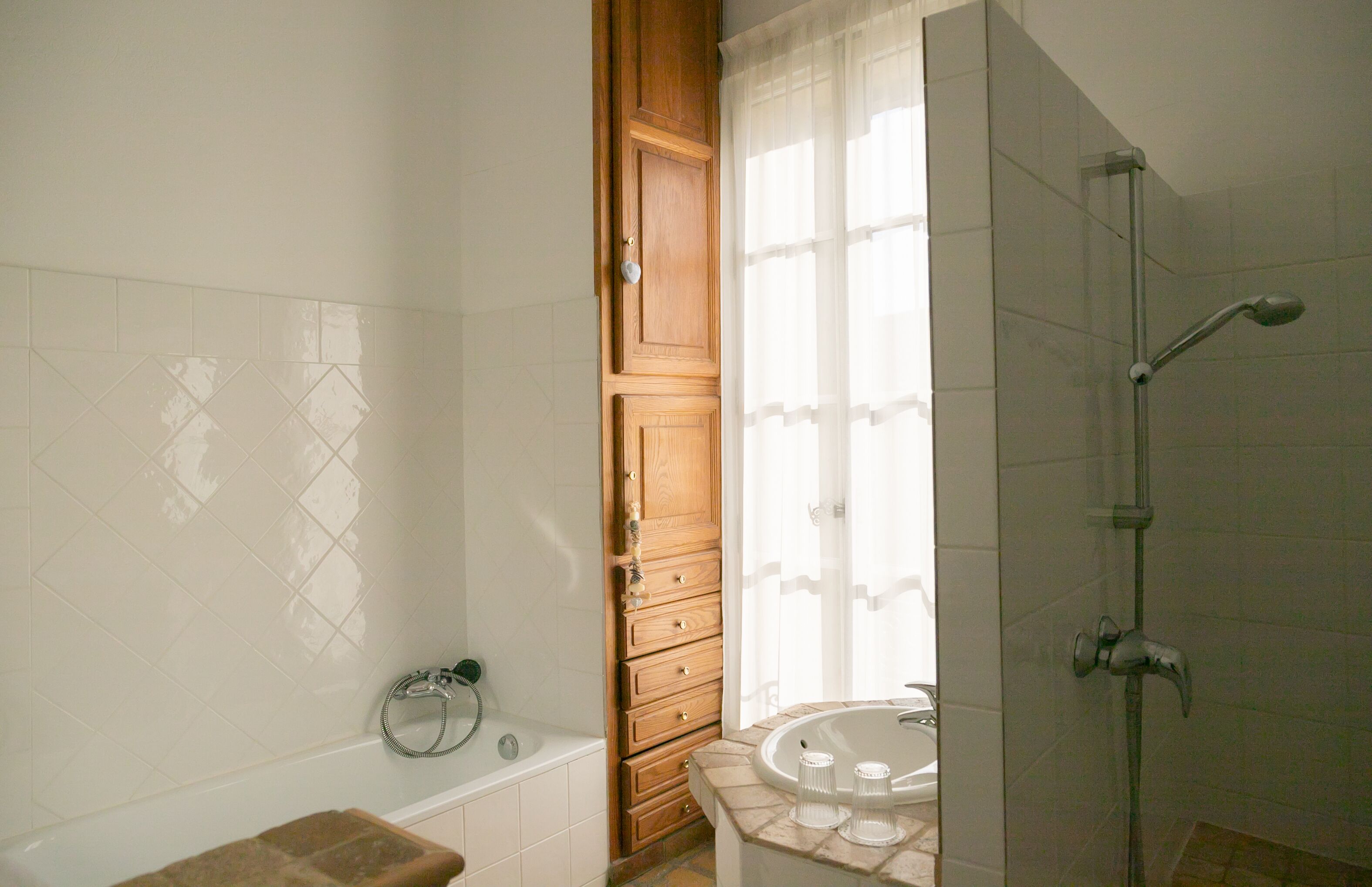 A bathroom with a bathtub, shower, and wooden cabinet.