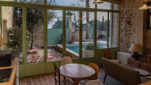 Un comedor acogedor con una mesa y sillas, un sofá, y vistas a una piscina y jardín a través de amplios ventanales.