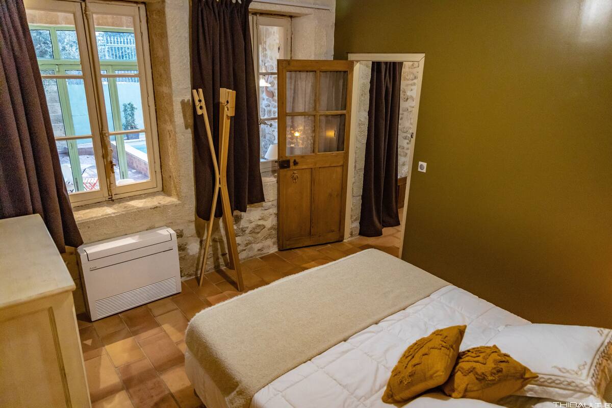 A bedroom with a bed, a wooden door, a window with curtains, and a radiator.