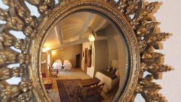 Ein Spiegel mit aufwendiger Rahmung spiegelt ein Zimmer mit einem Bett, einem Sessel und einem Tisch wider.
