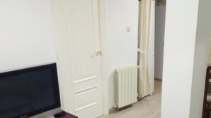 Ein Wohnzimmer mit einem Flachbildfernseher auf einem Holzboden, einem Glastisch und einer weißen Tür im Hintergrund.