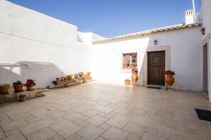 A courtyard with a tiled floor, white walls, a wooden door, and potted plants.