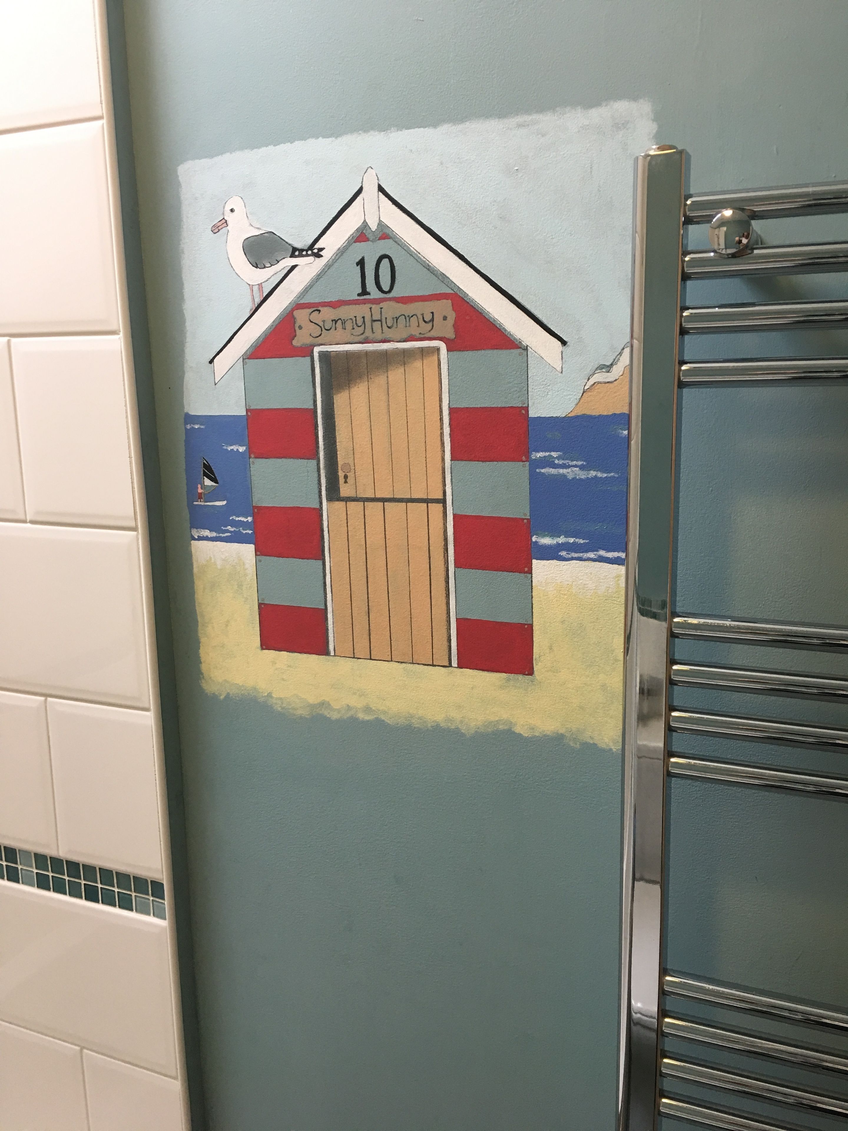 A bathroom with a wall mural of a beach hut labeled "Sunny Hunny" and the number "10".