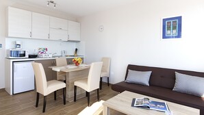 A modern living room with a brown sofa, a coffee table, and a dining area with chairs and a small kitchen. - Villa Ragusa Palace-Funjestra (Dubrovnik)