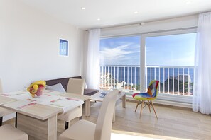 A dining area with a table set for four, a colorful chair, and a view of the sea through large windows.