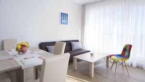 A modern living room with a sofa, a dining table with placemats, a colorful chair, and a window with sheer curtains. - Villa Ragusa Palace-Funjestra (Dubrovnik)