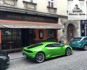 A green sports car parked in front of a building with a sign that reads "RESTOBAR OLDSMOBIL RESTAURANT." - Oldsmobil-Aparts (Kraków)
