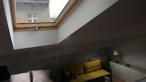 Ein Zimmer mit Oberlicht, einem Bett, einem gelben Sofa, einem Nachttisch und einer Lampe.