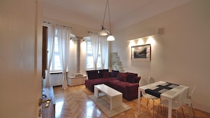 Ein modernes Wohnzimmer mit Holzboden, einem roten Sofa, einem weißen Couchtisch, einem Esstisch mit Stühlen und einer Treppe, die in einen anderen Raum führt.