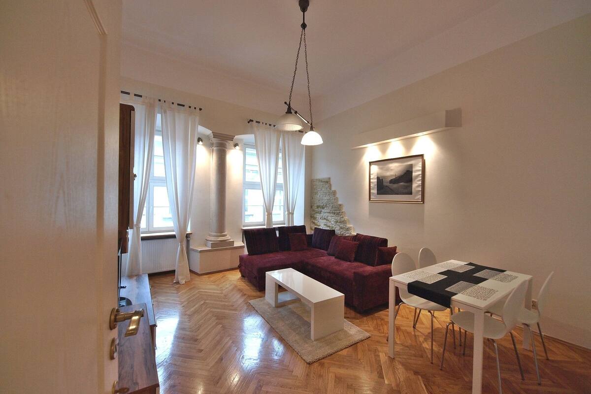 Ein modernes Wohnzimmer mit Holzboden, einem roten Sofa, einem weißen Couchtisch, einem Esstisch mit Stühlen und einer Treppe, die in einen anderen Raum führt.