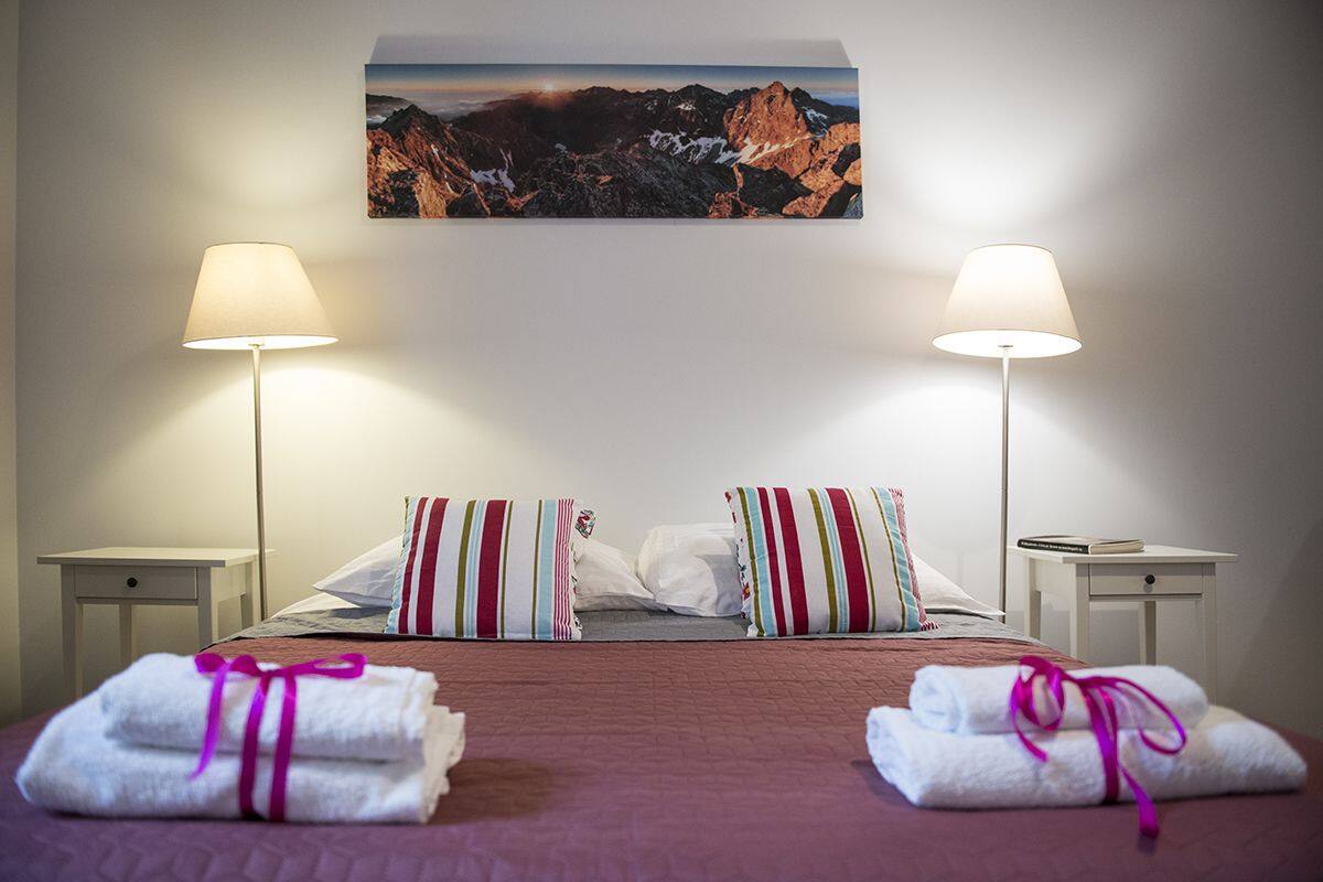 Ein Hotelzimmer mit einem Bett, zwei Nachttischlampen, einem Gemälde mit Berglandschaft und Handtüchern auf dem Bett.