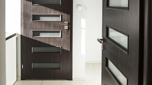 Ein modernes Interieur mit einer dunklen Holztür, die mehrere rechteckige Glasscheiben und einen Metallgriff aufweist.