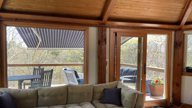A cozy living room with a sectional sofa, a small round table, and a view of the outdoor deck through large windows.