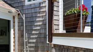A wooden exterior wall with a window and a metal showerhead.