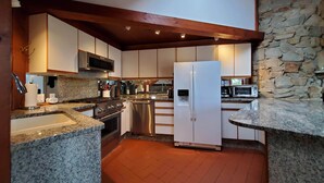 A modern kitchen with granite countertops, stainless steel appliances, and a stone wall.
