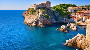 A coastal town with a historic stone castle on a rocky outcrop, surrounded by lush greenery and traditional buildings. - Apartments Ragusa Palace- Dardin (Dubrovnik)