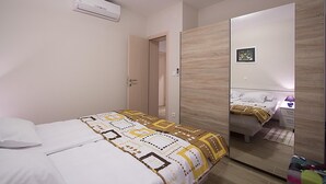 A bedroom with a bed, a wardrobe, a mirror, and an air conditioning unit. - Apartments Ragusa Palace- Dardin (Dubrovnik)