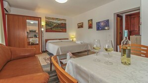 Ein Hotelzimmer mit einer Couch, einem Esstisch mit Weingläsern, zwei Betten und Kunstwerken an den Wänden.