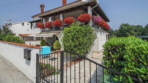 Ein zweistöckiges Haus mit Balkon, geschmückt mit roten Blumen, heller Fassade und Ziegeldach.