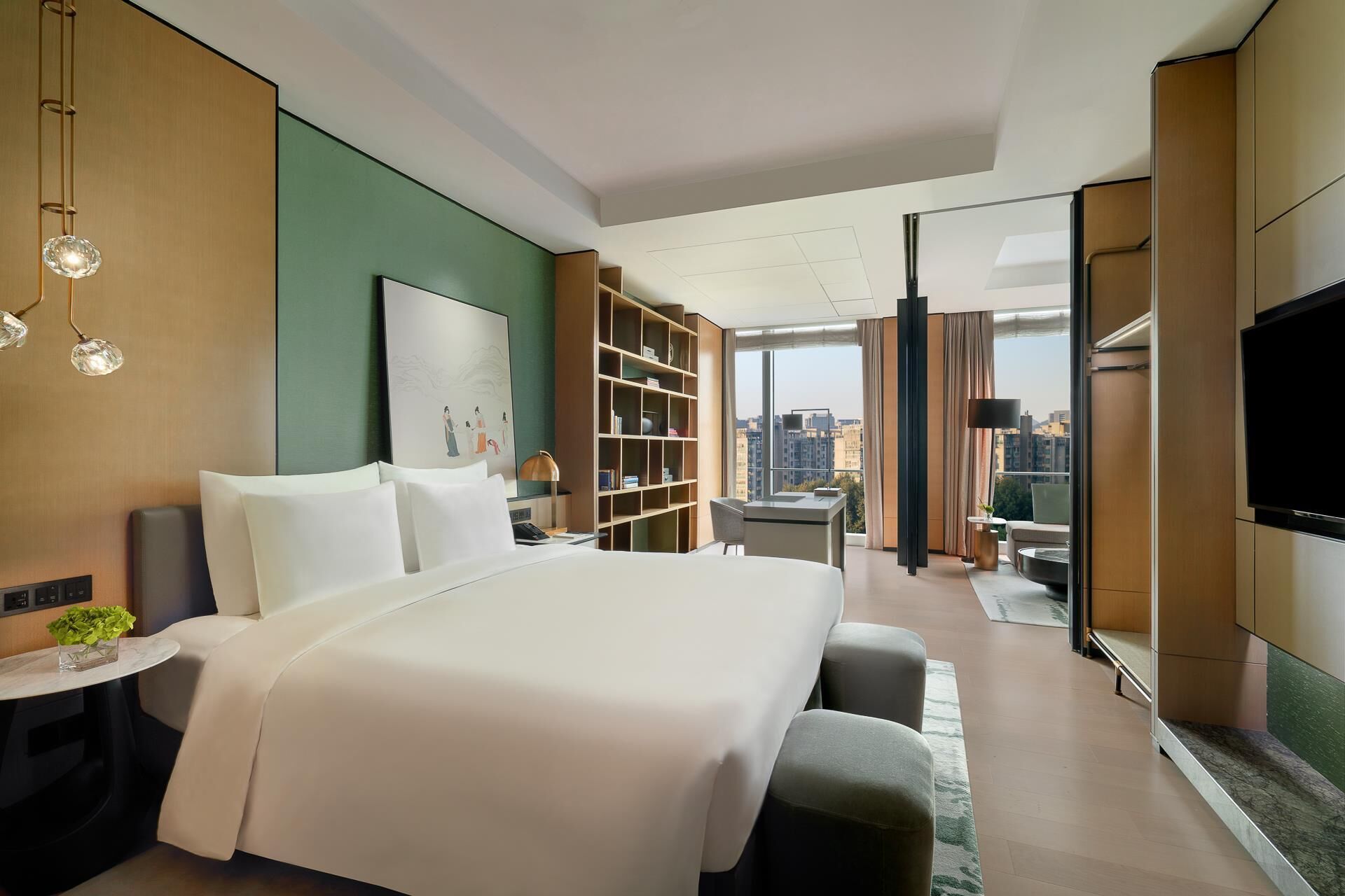 A modern hotel room with a large bed, a desk, a bookshelf, a TV, and a city view.