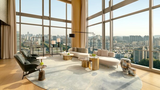 A spacious living room with large windows, a sofa set, a coffee table, and a floor lamp.