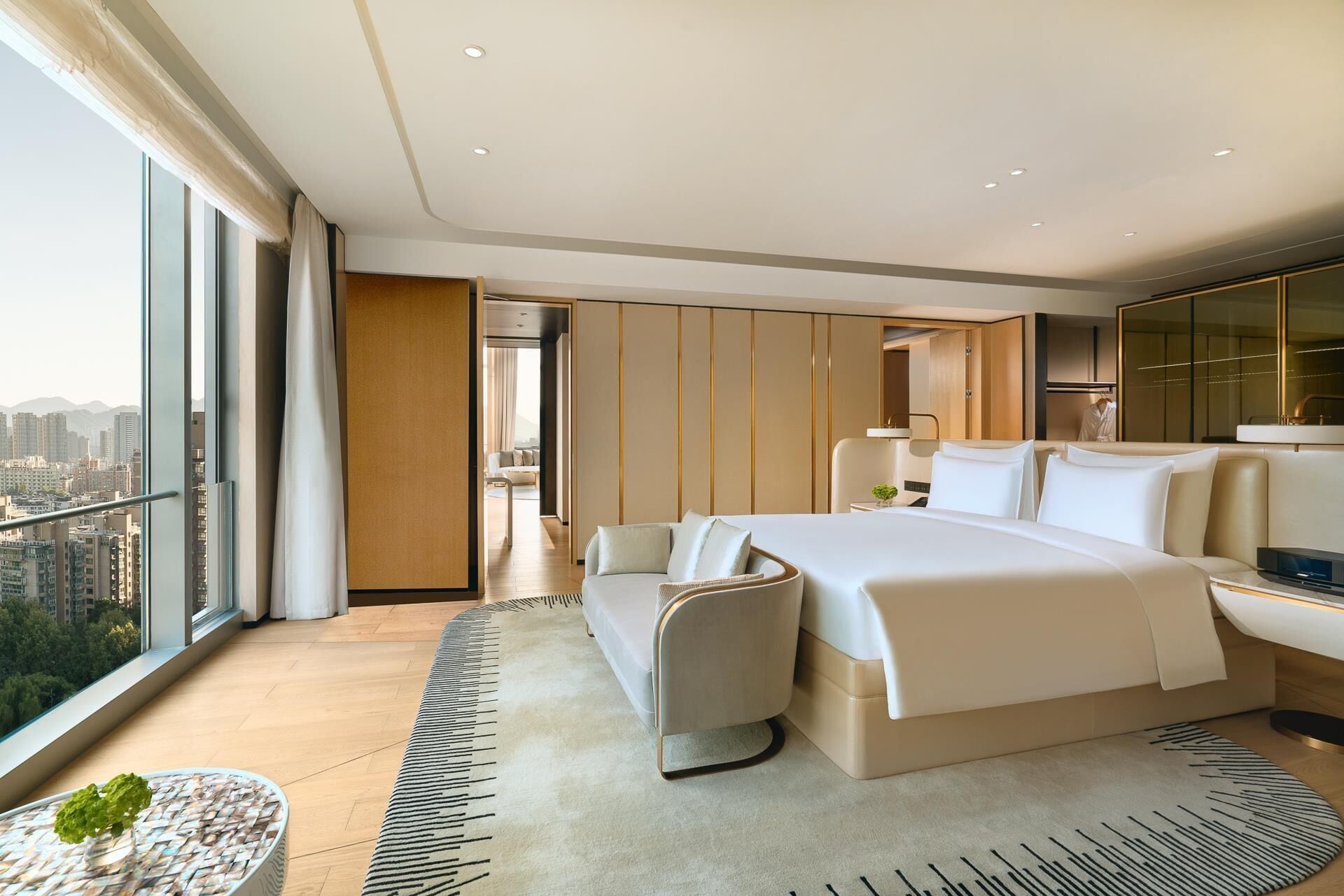A modern hotel room with a large bed, a seating area, and a view of the city.
