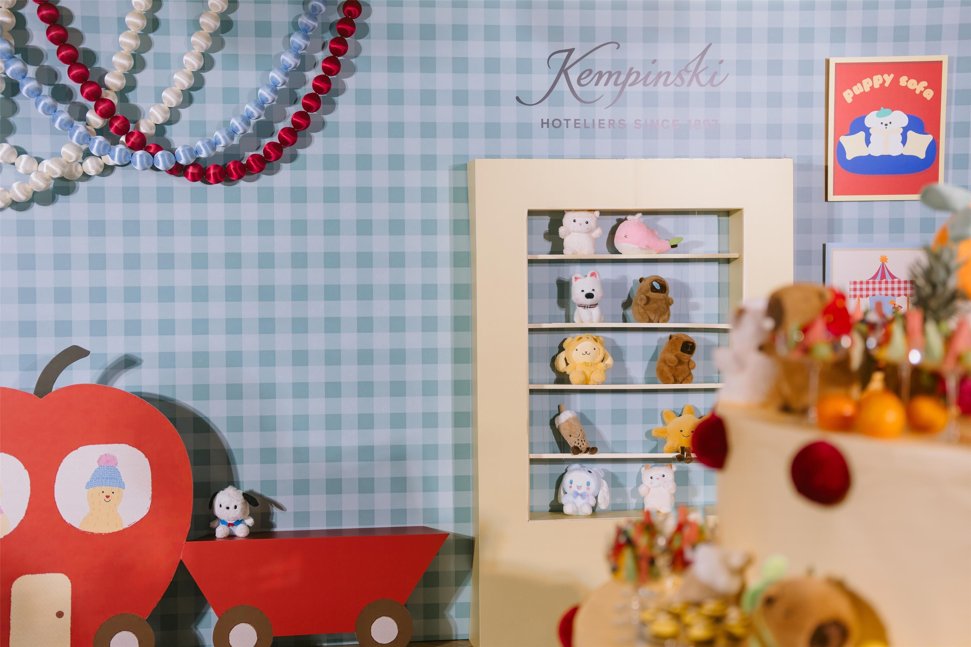 A room with a checkered wall, a shelf with plush toys, and a red toy train.