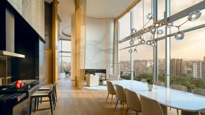 A modern dining area with a large table and chairs, a kitchen area with a stove, and large windows offering a city view.