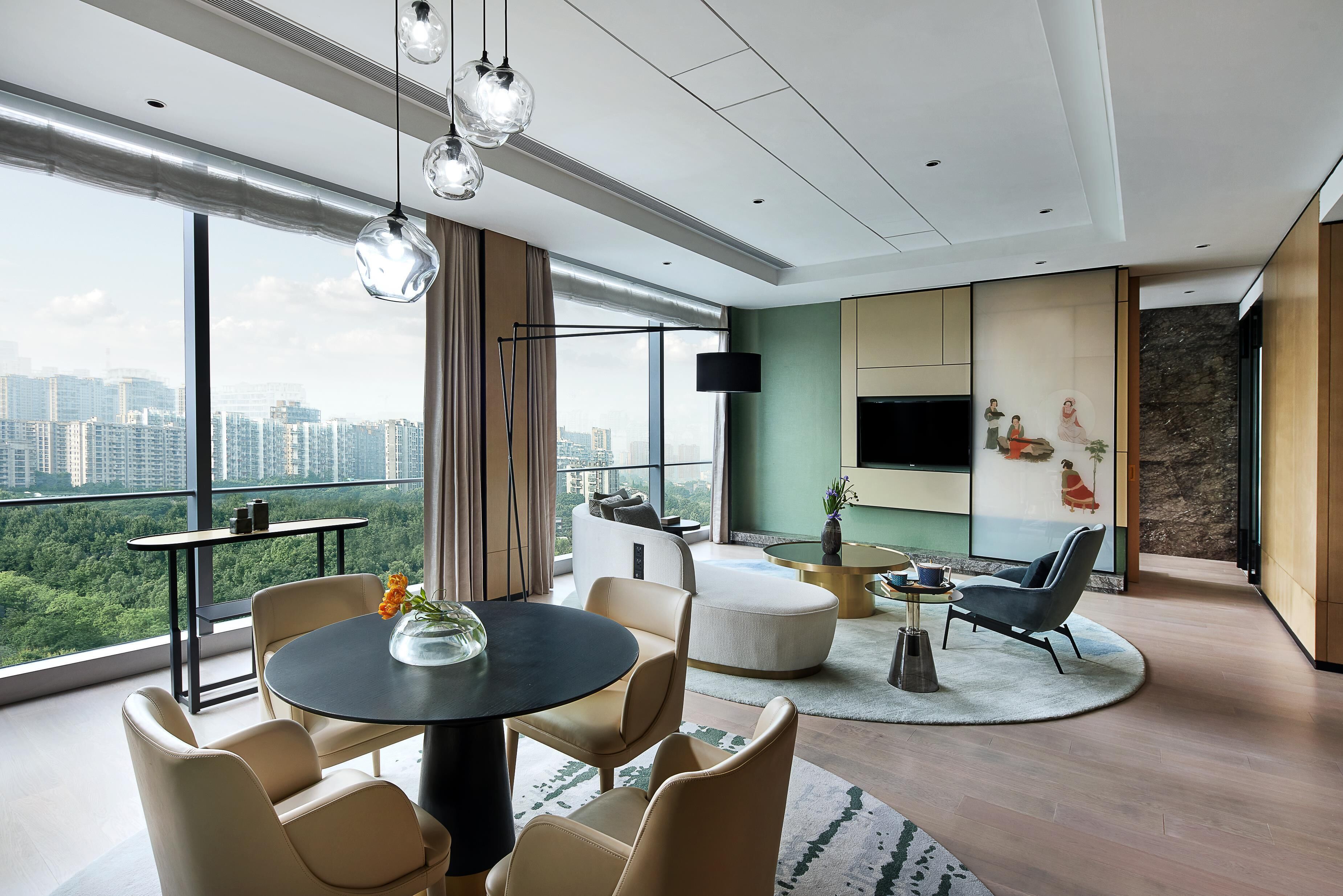 A modern living room with a large window, a round table, and comfortable seating.