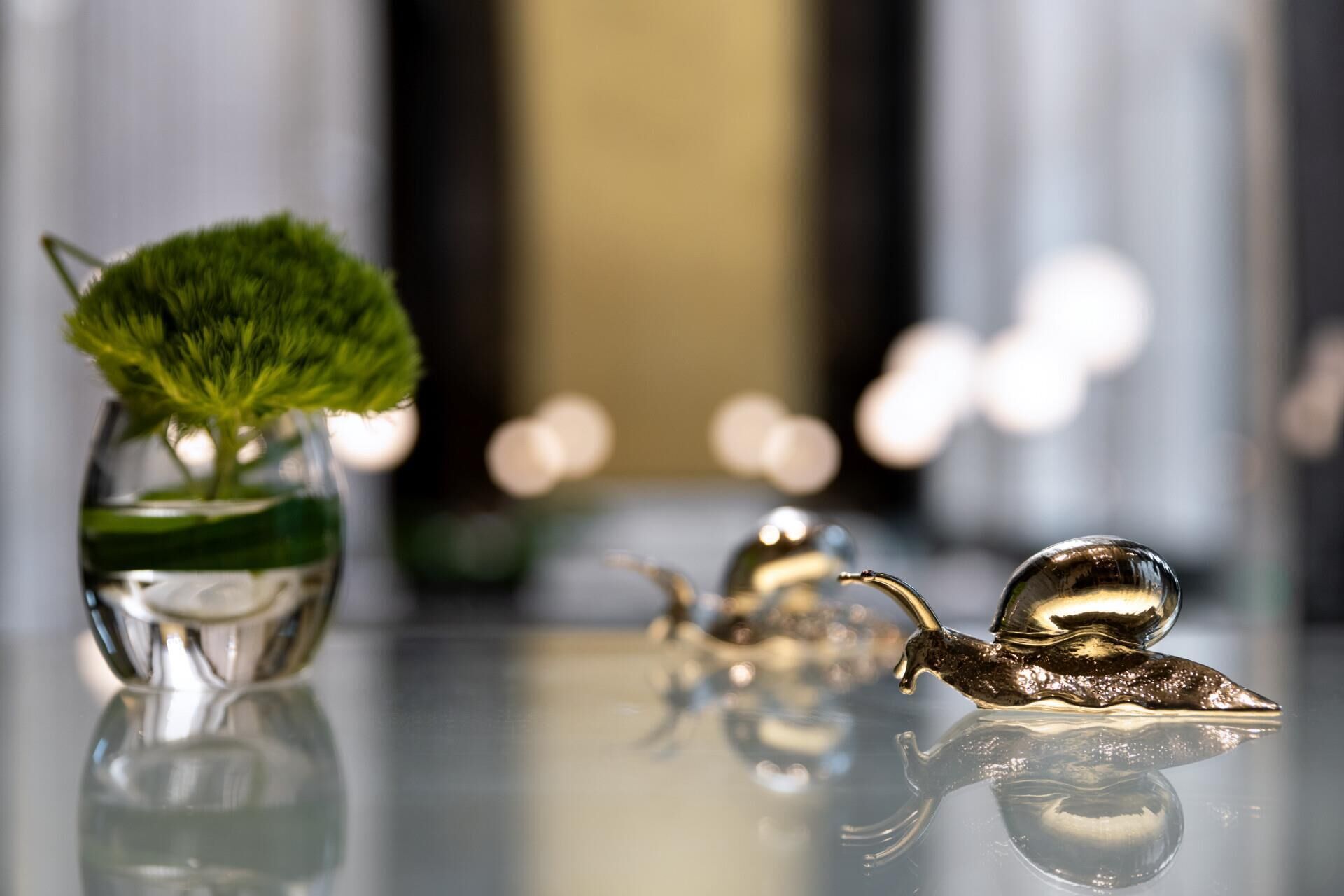 A table with a glass vase containing a plant and two metallic snail figurines.
