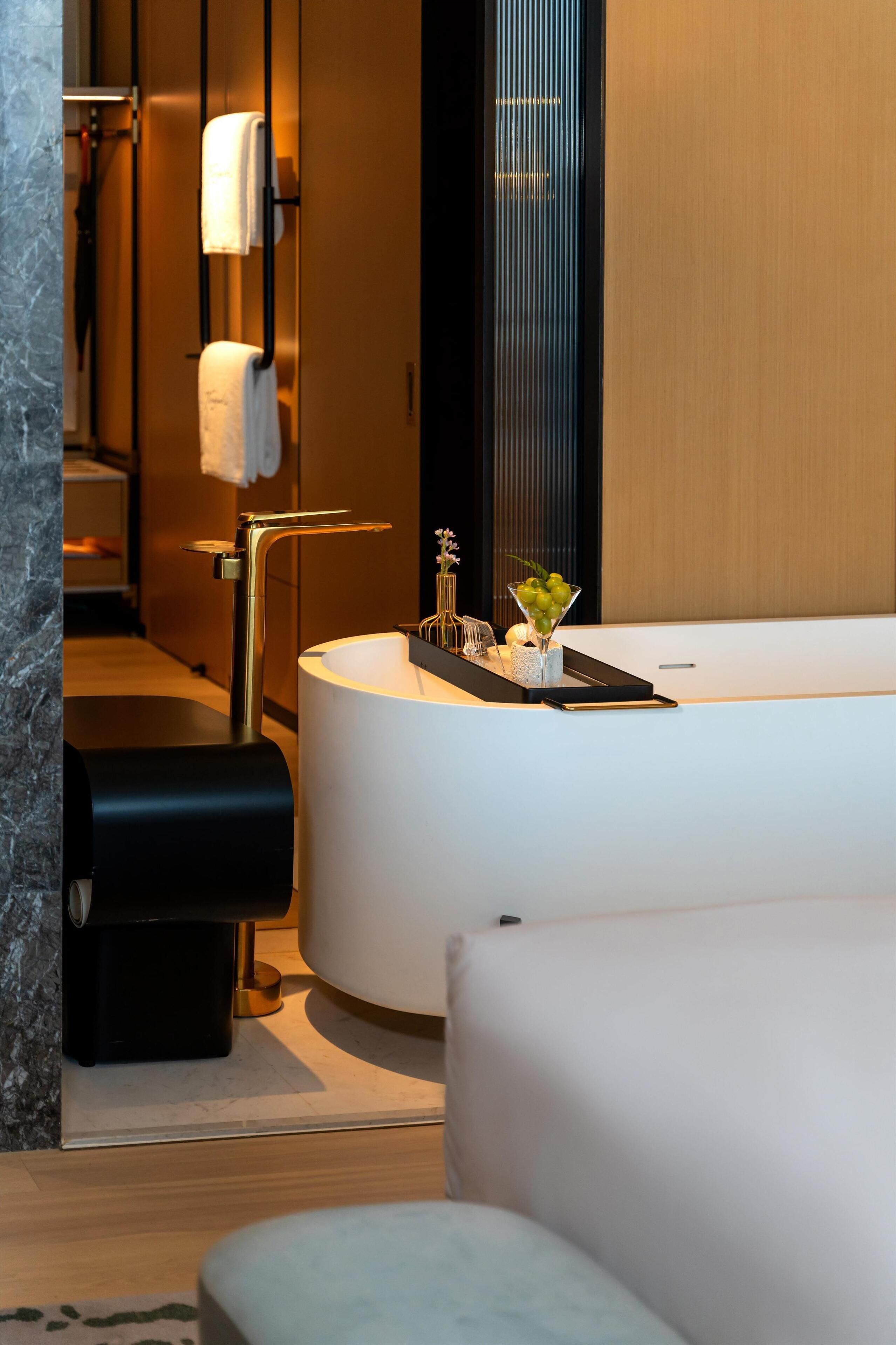 A modern bathroom with a large bathtub, a round sink, and a towel rack.