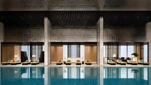 A modern indoor pool area with lounge chairs and a clear reflection on the water.