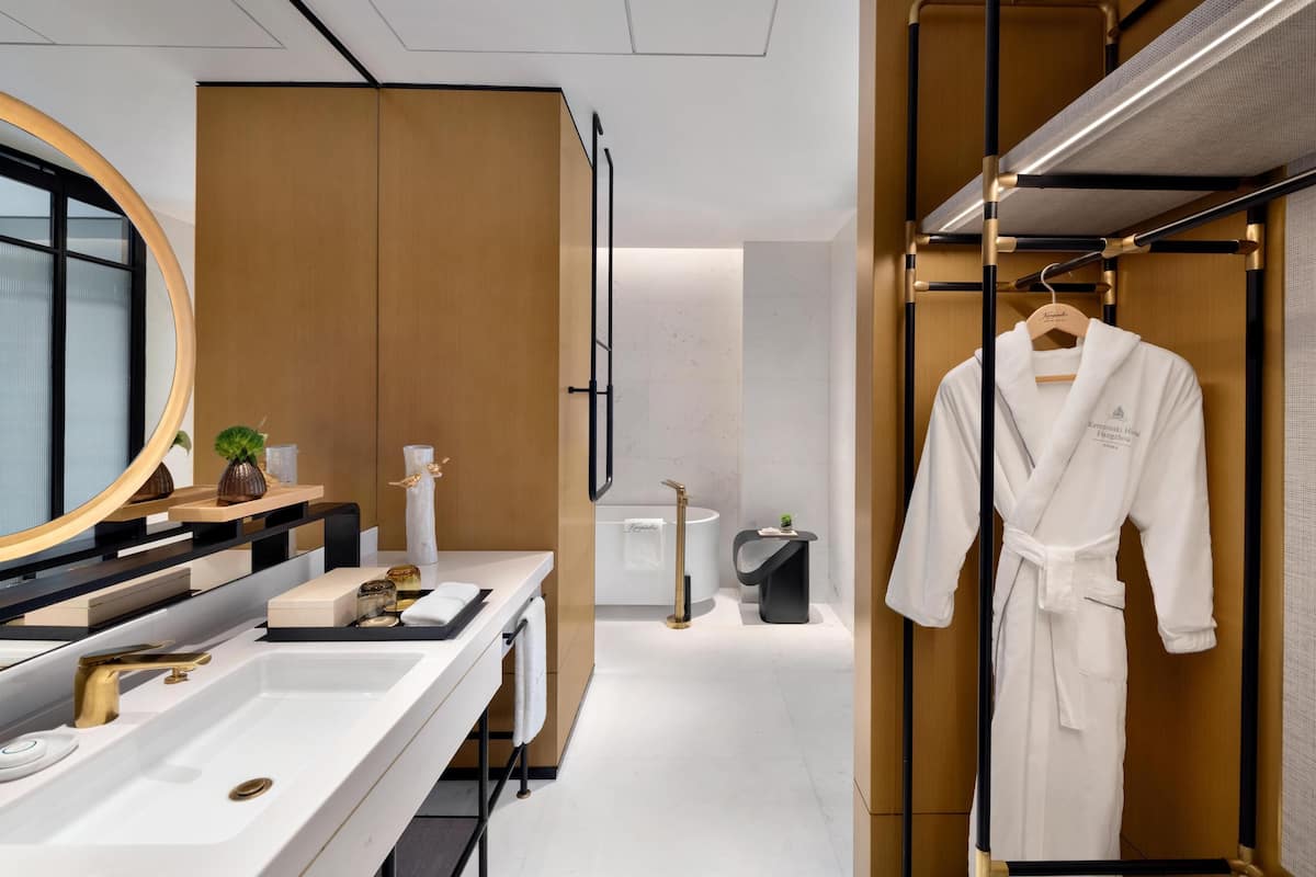 Un baño moderno con un espejo grande, un lavamanos blanco, un grifo dorado y una bata colgada en un perchero.