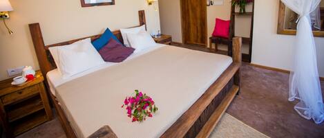 A neatly made bed with a white comforter and a bouquet of flowers. There is a wooden headboard, a nightstand with a lamp, and a wooden chair.