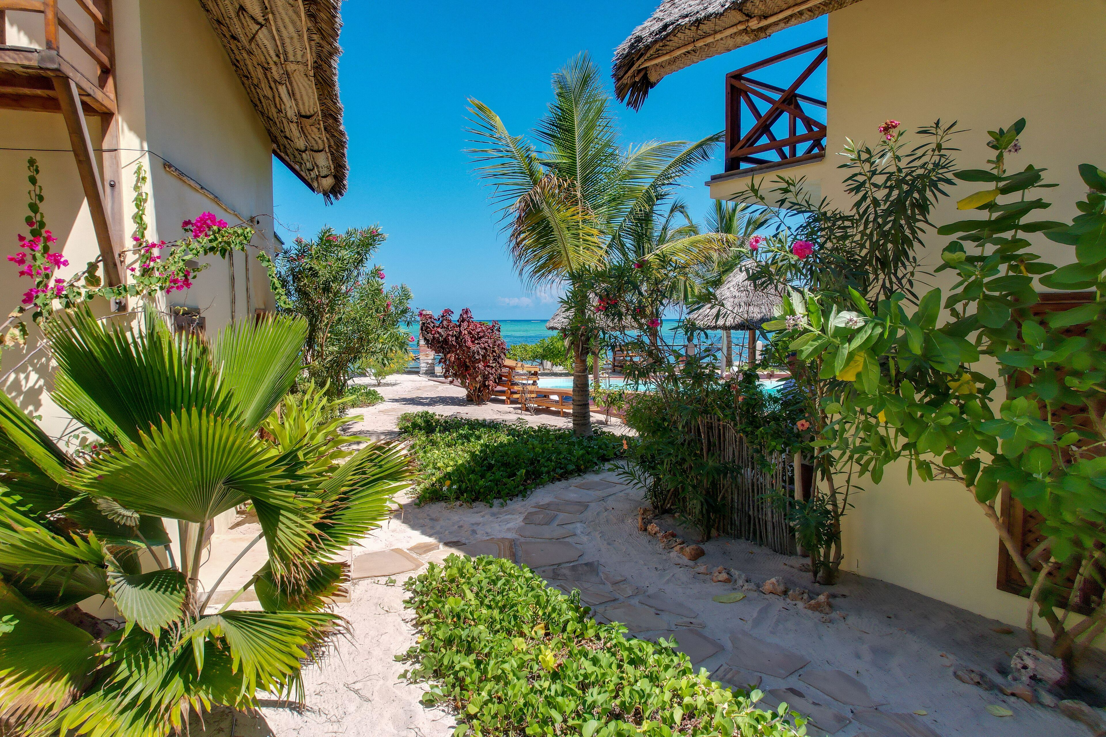 A tropical garden path leading to a pool area with a view of the ocean.
