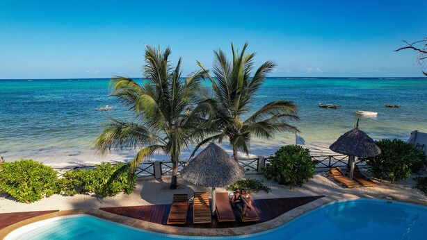 A poolside area with lounge chairs, a thatched umbrella, and palm trees. - Clove Island Villas & SPA (Makunduchi)