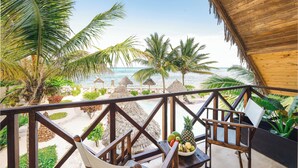 A balcony with a wooden railing overlooking a beach with palm trees and a wooden hut. - Clove Island Villas & SPA (Makunduchi)
