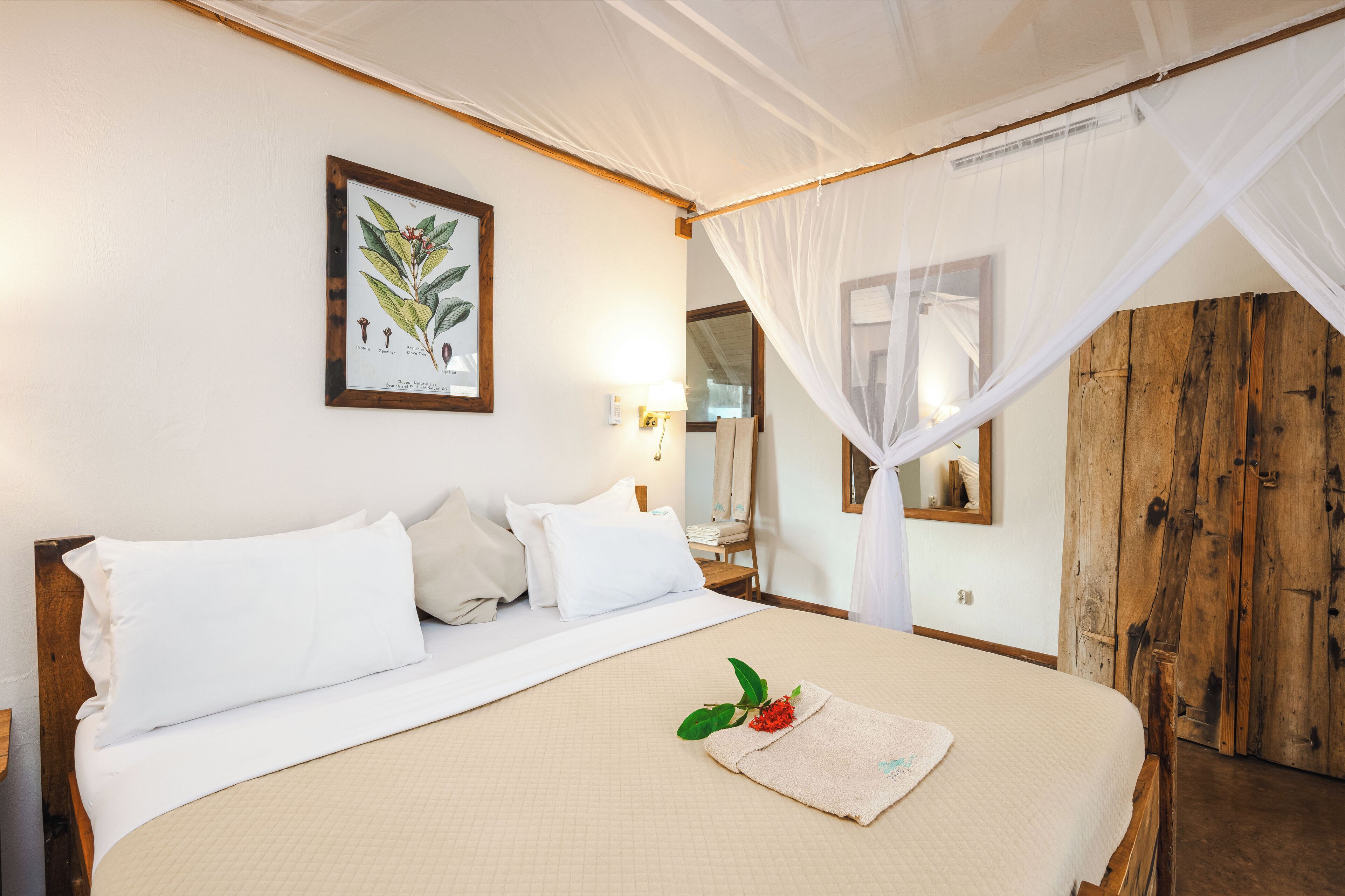 Uma cama bem arrumada com lençóis brancos, uma ilustração botânica emoldurada na parede e um guarda-roupa de madeira.