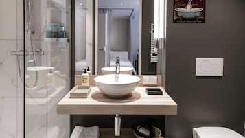 A modern bathroom with a glass-enclosed shower, a large mirror, a white sink, and a toilet.