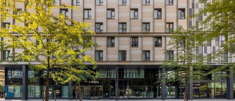 Un bâtiment moderne avec une façade composée d’une grille de fenêtres et une enseigne indiquant « Adina » au rez-de-chaussée.