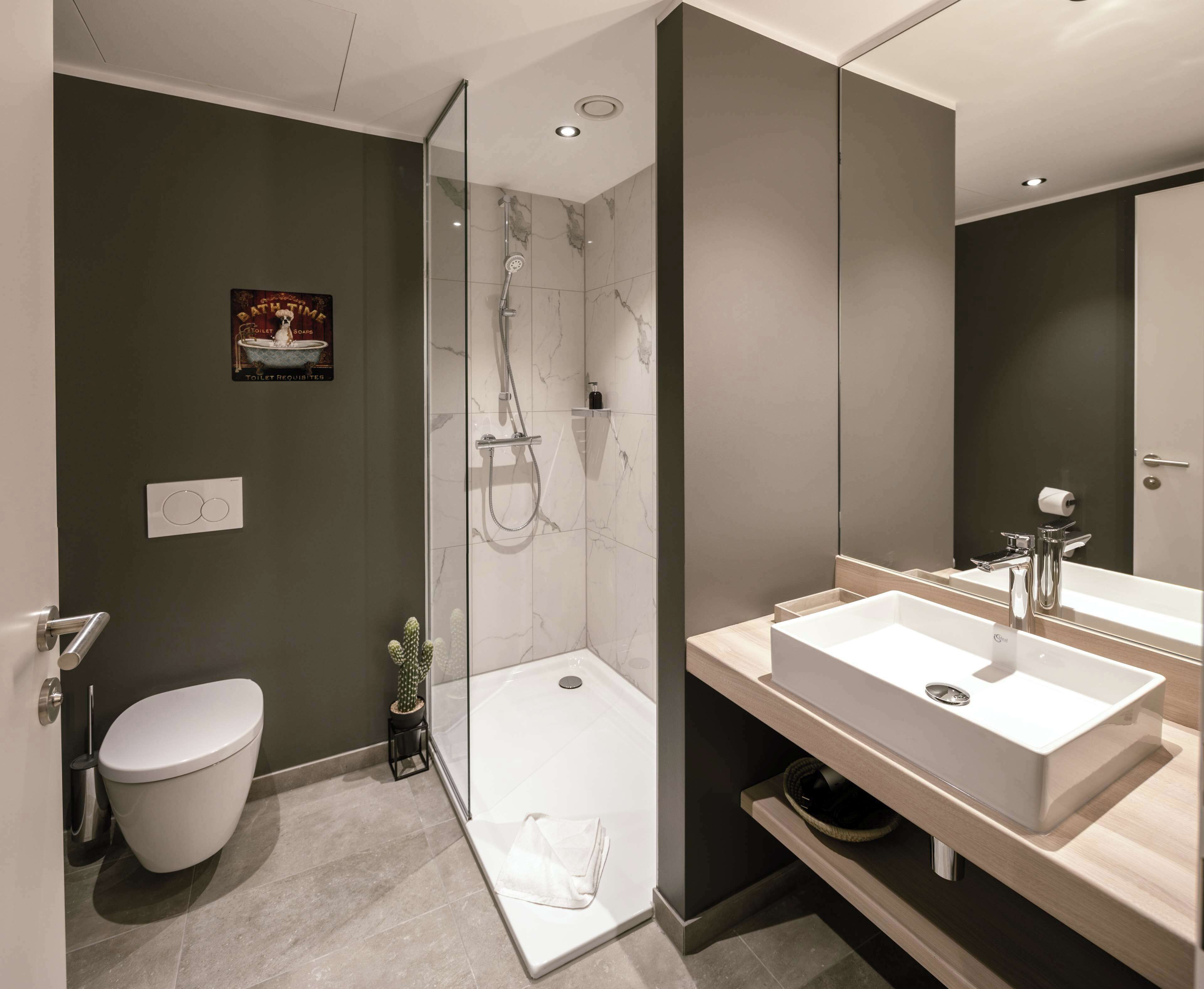 Un baño moderno con ducha de vidrio, inodoro blanco y un espejo grande sobre un lavabo blanco.