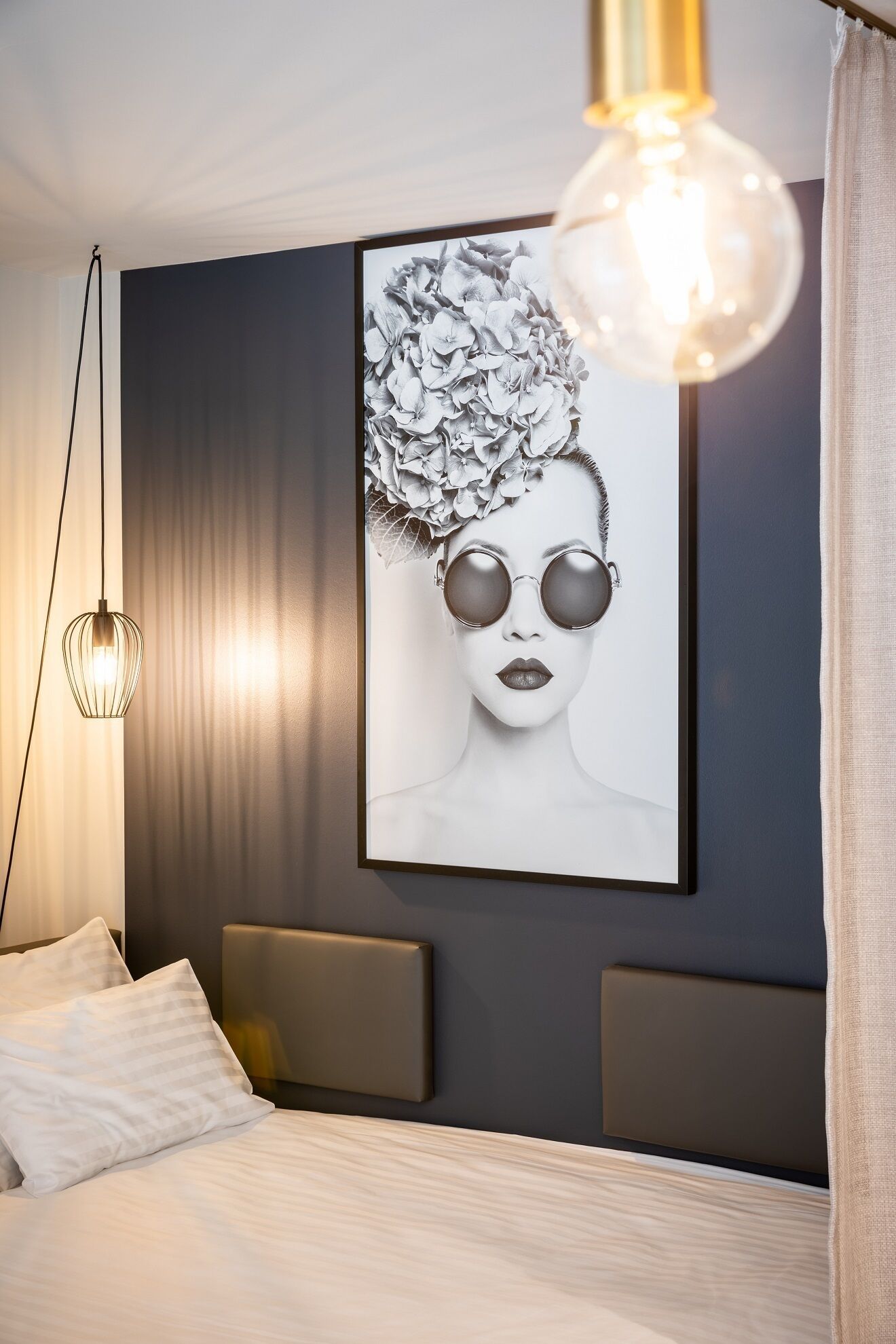 A modern bedroom with a large framed artwork, a hanging light fixture, and a bed with a headboard.