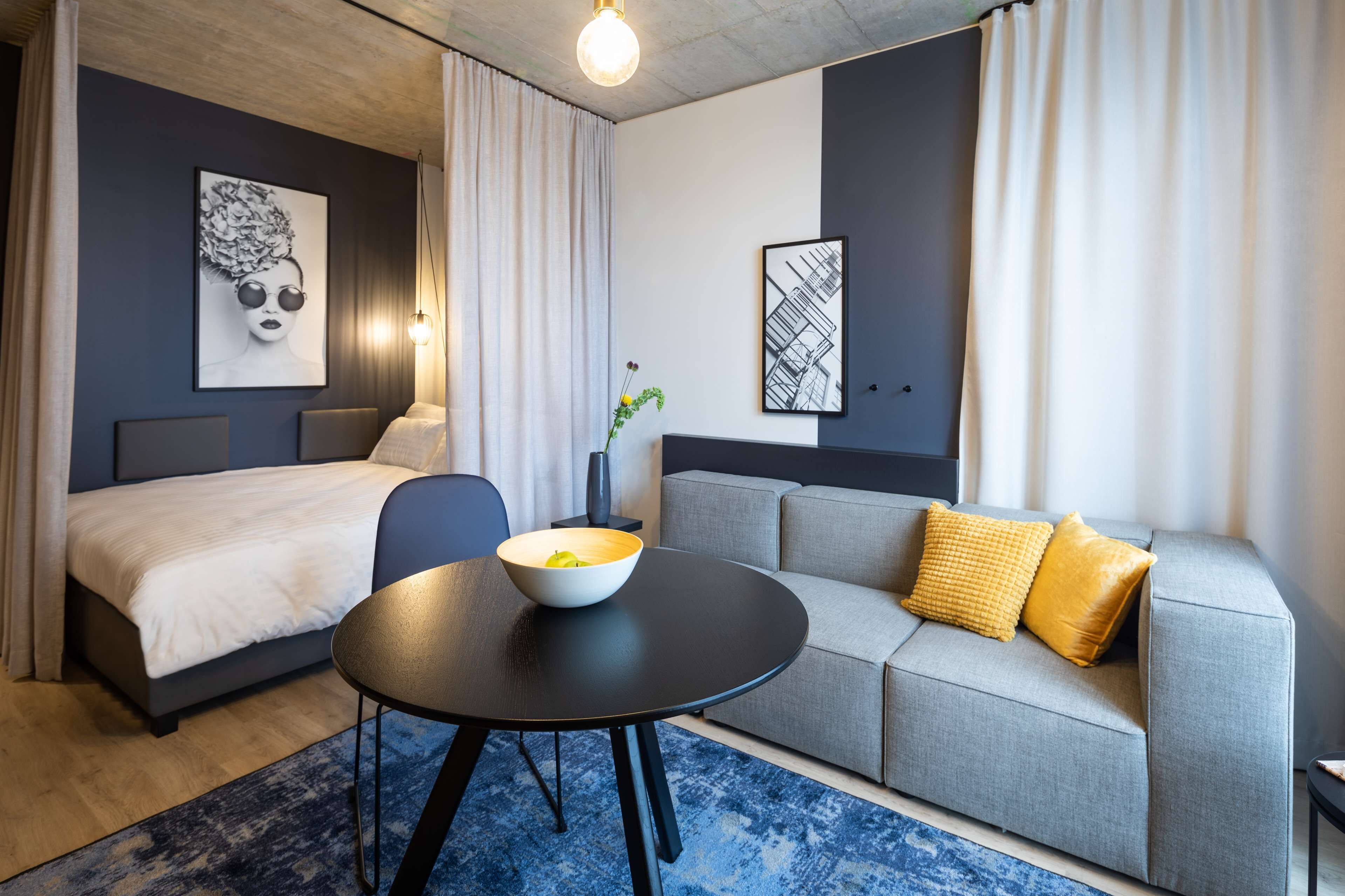 Ein modernes Hotelzimmer mit Bett, einer Couch, einem runden Tisch mit Schale und einer Pflanze in einer Vase.